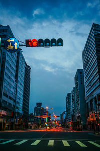 Road signal on city street amidst buildings against cloudy sky