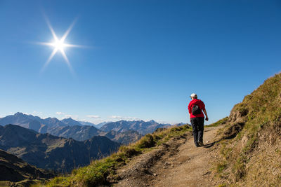 Rear view of woman walking on mountain against blue sky