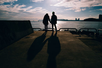 Silhouette people standing on beach in city against sky