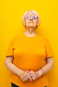 Portrait of woman with arms raised against yellow background