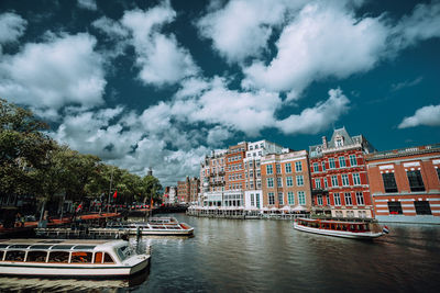 Boats on canal by buildings against cloudy sky in city