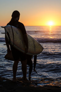 Rear view of man standing at beach during sunset