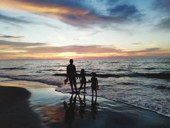 Silhouette people on beach against sky during sunset