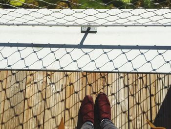 Low section of person standing by fence with shadow