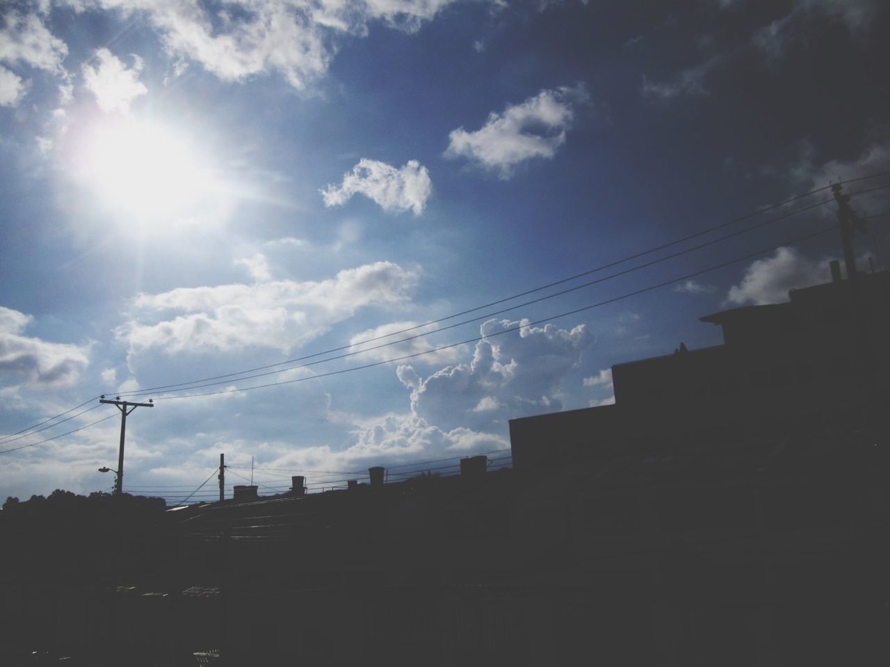 sky, low angle view, sun, building exterior, fuel and power generation, cloud - sky, built structure, sunlight, architecture, sunbeam, cloud, electricity, silhouette, electricity pylon, power line, outdoors, nature, technology, no people, vapor trail
