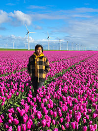 Rear view of woman standing amidst flowering plants on field against sky