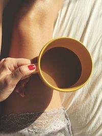 Close-up of woman holding coffee cup on bed