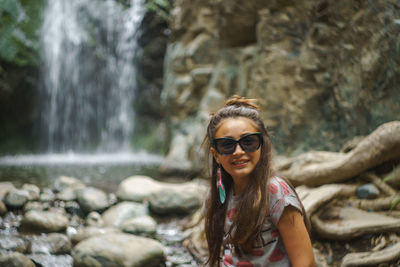 Portrait of smiling young woman against waterfall