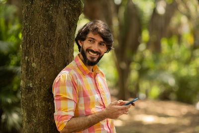 Young man with smartphone at day time with a green park in the background. mobile phone, technology,