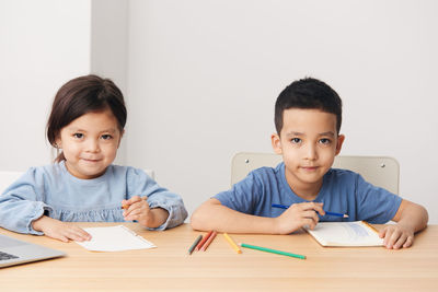 Smiling girl and brother drawing on paper at home