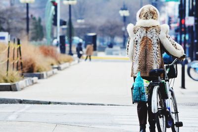 Rear view of woman in warm clothing with bicycle walking on street