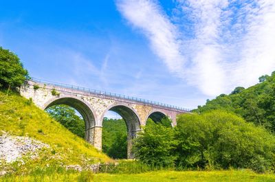 Arch bridge over grassy field against sky