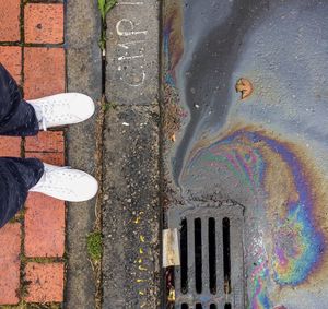 Low section of man standing by oil spill on street