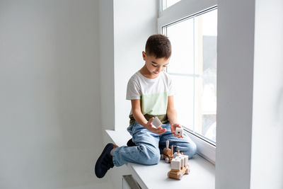 A preschooler boy plays with a wooden toy train on the windowsill