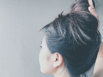 Rear view of young woman tying hair bun against gray wall