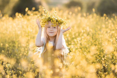 Cute child girl 4-5 year old wear floral wreath stand in yellow flower meadow outdoor over nature