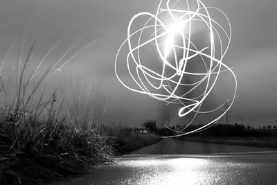 Light trails by lake against sky at night