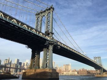 Low angle view of manhattan bridge over east river in city against blue sky