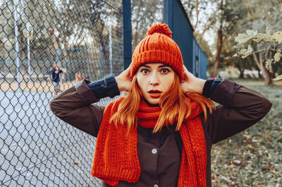 Bright cute young woman in orange warm knitted hat and scarf hands near head. emotion of concern.