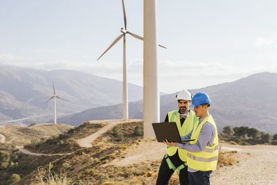 Technician and engineer working on laptop in front of wind turbines