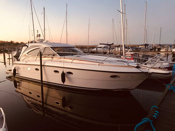 Sailboats moored in harbor at sunset