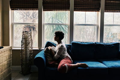 Teenage girl sitting on sofa by window at home