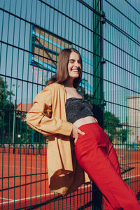 Portrait of smiling young woman standing against fence