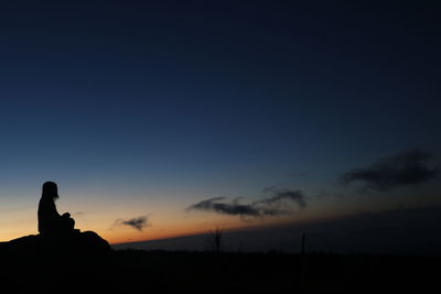 Silhouette people sitting on field against sky during sunset