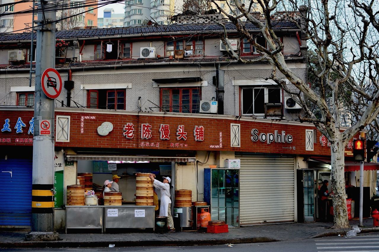 architecture, built structure, building exterior, text, western script, non-western script, communication, city, day, hanging, outdoors, graffiti, tree, store, railing, building, incidental people, entrance, residential building, no people