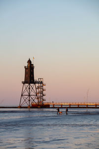 Lighthouse by sea against clear sky during sunset