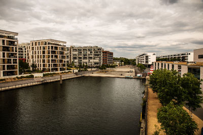 Buildings by river against sky in city