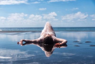 Rear view of shirtless man swimming in sea against sky
