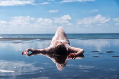 Woman lying at beach against sky