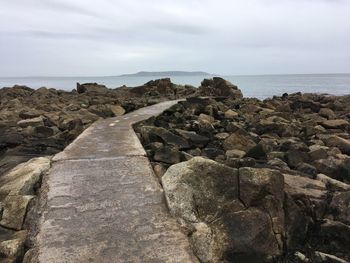 Rocks on shore by sea against sky