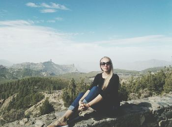 Woman sitting on retaining wall against sky