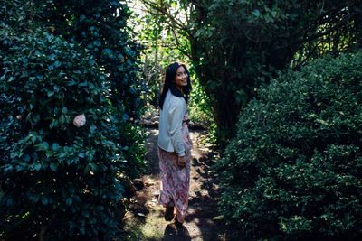 Rear view portrait of happy woman walking amidst plants at park