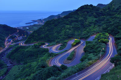 High angle view of light trails on road by mountain against sky