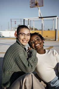 Friends smiling while sitting at basketball court