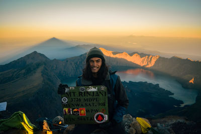 Portrait of smiling young woman standing on mountain against sky