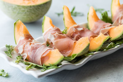 Cantaloupe wedges wrapped in prosciutto deli meat on a bed of arugula.