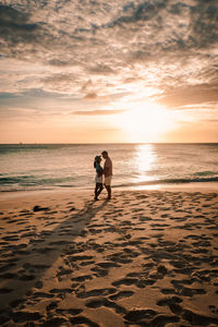 Couple standing on beach against sky during sunset