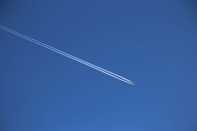 Low angle view of vapor trails against clear blue sky