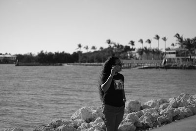 Side view of woman standing near beach looking out at water