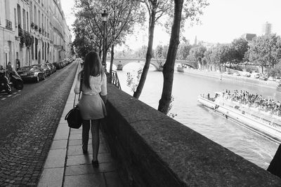 Rear view of woman walking on footpath by seine river