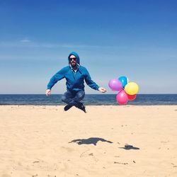 Full length of man in mid-air with multi colored balloons at beach