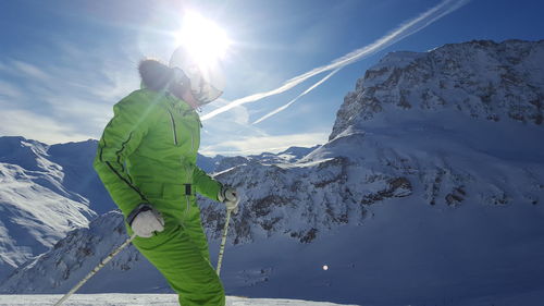 Man skiing by snowcapped mountains against sky on sunny day