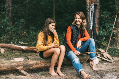 Group of kids with mom sitting by the fire and drinking tea in autumn forest, hike at weekend