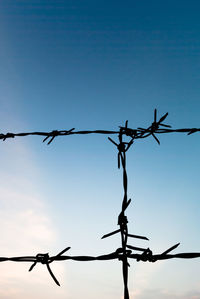 Low angle view of silhouette barbed wire fence against sky