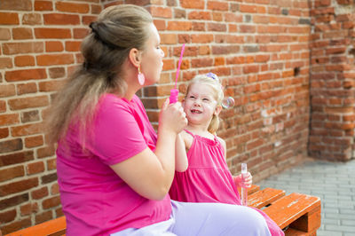 Side view of mother and daughter sitting on brick wall