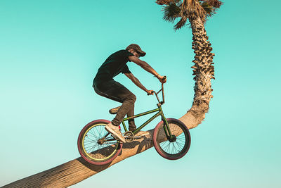 Low angle view of man jumping bicycle against clear sky